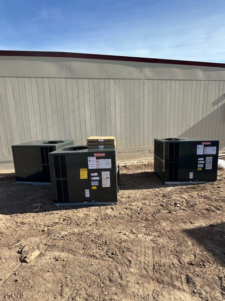 Three Goodman packaged HVAC units set on the ground beside a modular building