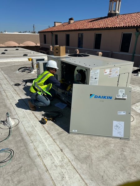 Technician in a hard hat and safety vest servicing a Daikin rooftop unit