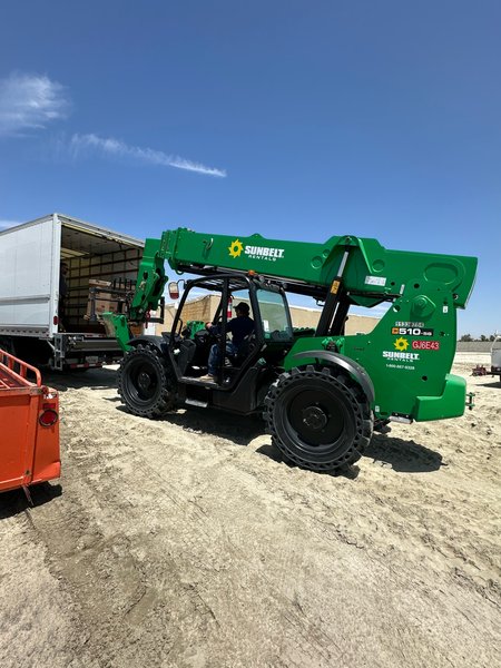 Telehandler unloading HVAC equipment from a delivery truck on a job site